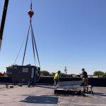 large crane on roof lifts A/C unit to two roof workers