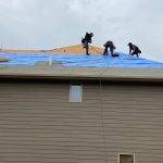three men work on brown house's roof